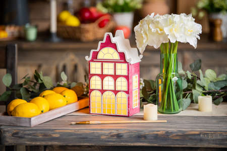 toy decorative lamp house stands on a wooden table among spring flowers and interior elements.の写真素材