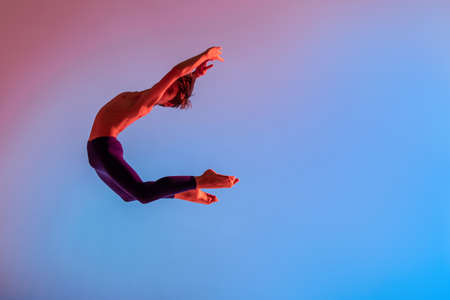 Slender teen ballet boy jumps barefoot under colored light.の写真素材