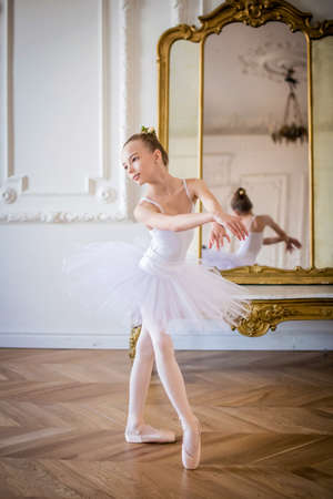 young slender ballerina in a white tutu dances on pointe shoes in a spacious, bright room with large windows.の写真素材