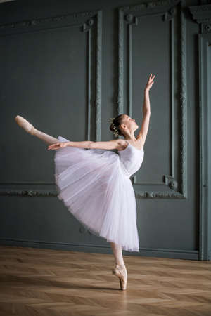 young slender ballerina in a white tutu dances on pointe shoes in a spacious, bright room with large windows.の写真素材