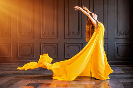 An elegant ballerina in pointe shoes dances with a flowing yellow fabric on a dark gray backgroundの写真素材