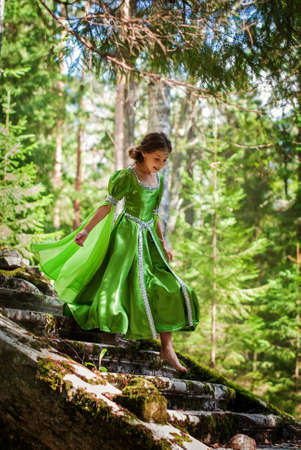 girl in a fairytale elf dress walks barefoot through the forest going down the runes of an ancient staircaseの写真素材