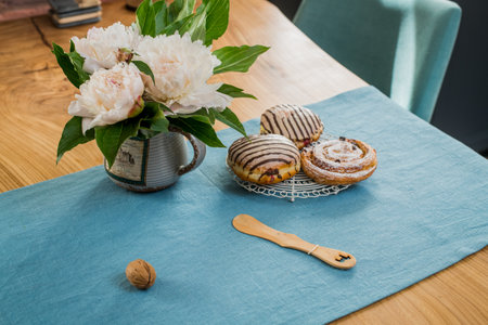 on a blue linen napkin on a wooden table there is a bouquet of delicate pink peonies and sweet buns lieの写真素材
