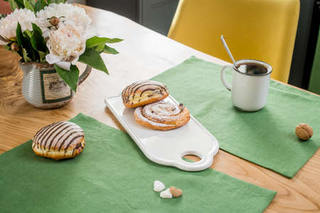 on a green linen towel on a wooden table there is a bouquet of delicate pink peonies and sweet buns lieの写真素材