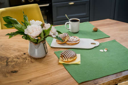 A bouquet of delicate pink peonies and sweet buns lie a wooden tableの写真素材