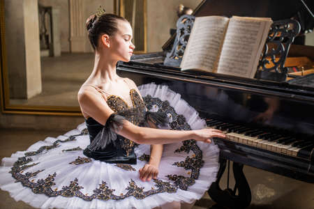 Young ballerina in a white tutu plays a beautiful old pianoの写真素材