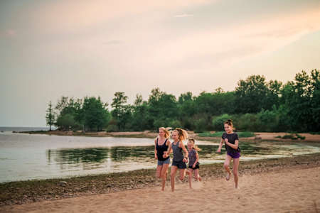 Children and adult girls run along the coast in sportswear on a background of nature at sunsetの写真素材