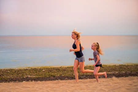 Children and adult girls run along the coast in sportswear on a background of nature at sunsetの写真素材