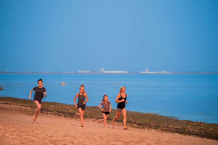 Children and adult girls run along the coast in sportswear on a background of nature at sunsetの写真素材