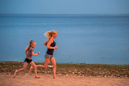 Children and adult girls run along the coast in sportswear on a background of nature at sunsetの写真素材