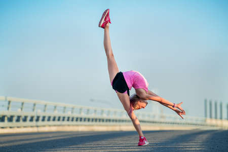Girl gymnast engaged in the summer on the street, on a background of blue sky, twine, stretching, arabesqueの写真素材