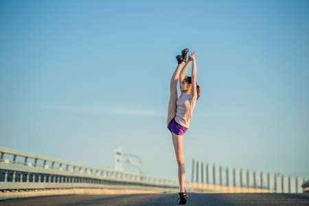 Girl gymnast engaged in the summer on the street, on a background of blue sky, twine, stretching, arabesqueの写真素材