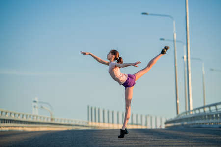 Girl gymnast engaged in the summer on the street, on a background of blue sky, twine, stretching, arabesqueの写真素材