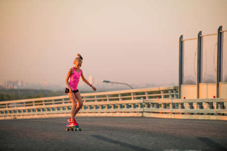 girl learns to ride a skateboard on the background of the evening city panoramasの写真素材