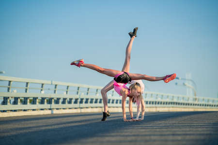 Two teenage girls perform an acrobatic element outdoors against a blue skyの写真素材