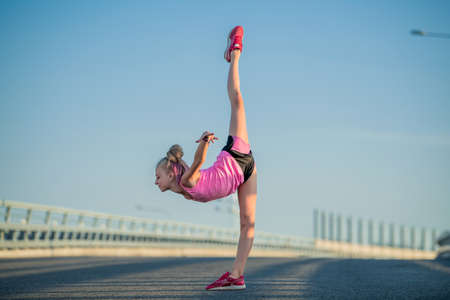 Girl gymnast engaged in the summer on the street, on a background of blue sky, twine, stretching, arabesqueの写真素材