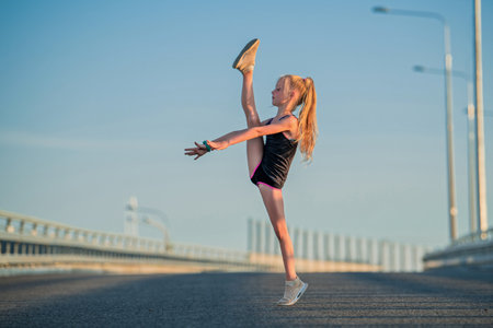 Girl gymnast engaged in the summer on the street, on a background of blue sky, twine, stretching, arabesqueの写真素材