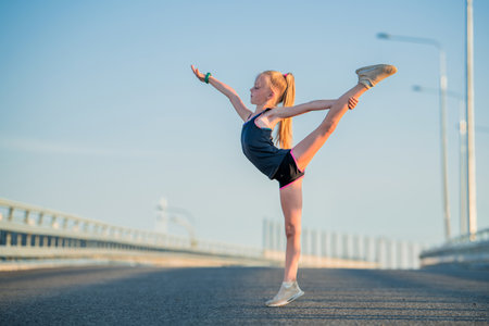 Girl gymnast engaged in the summer on the street, on a background of blue sky, twine, stretching, arabesqueの写真素材