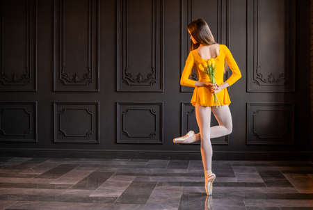elegant ballerina in pointe shoes dances with a bouquet of tulips on a dark gray backgroundの写真素材