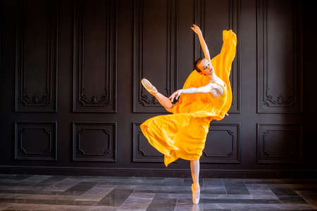An elegant ballerina in pointe shoes dances with a flowing yellow fabric on a dark gray background