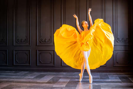 An elegant ballerina in pointe shoes dances with a flowing yellow fabric on a dark gray backgroundの写真素材