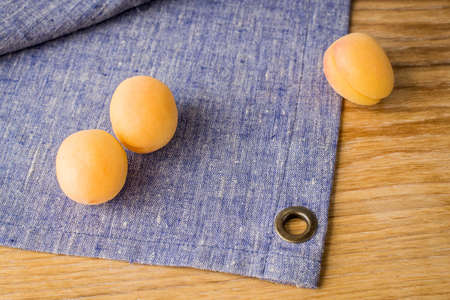 three ripe yellow apricots lie on a lilac linen napkin.の写真素材