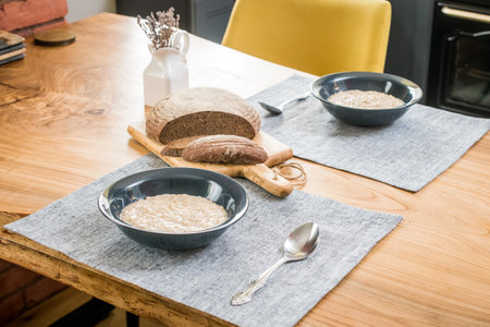 Two plates of oatmeal and sliced rye bread lie on the wooden tableの写真素材