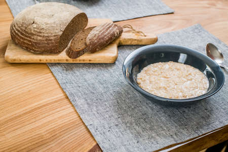 plate of oatmeal and sliced rye bread lie on a wooden tableの写真素材