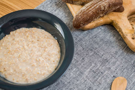 plate of oatmeal and sliced rye bread lie on a wooden tableの写真素材
