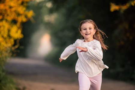 girl junior schoolgirl runs along the road in the evening in the park, happy face, bright emotions, hair is developing in the wind.の写真素材