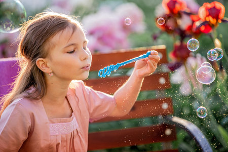 girl blows soap bubbles on the background of flowers in the garden. On the face of emotions of surprise and admiration.の写真素材