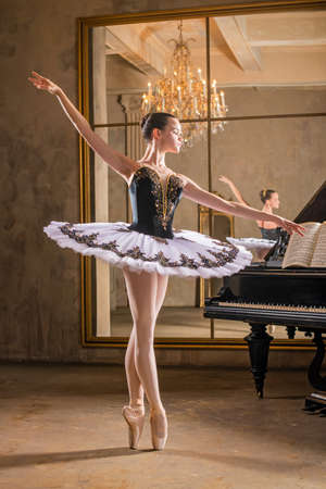 Young ballerina in a white tutu dancing on a beautiful old piano in a vintage interiorの写真素材