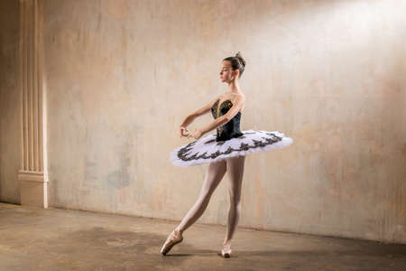 Young ballerina in a white tutu dancing in a spotlight in a vintage sceneの写真素材
