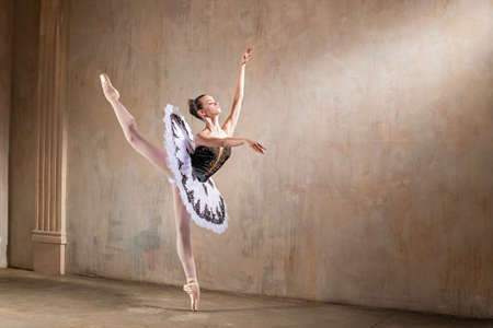 Young ballerina in a white tutu dancing in a spotlight in a vintage sceneの写真素材