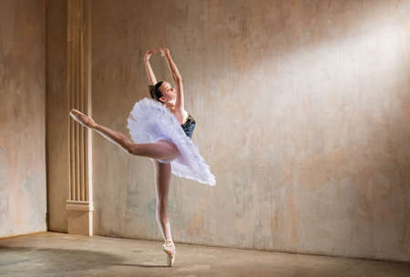 Young ballerina in a white tutu dancing in a spotlight in a vintage sceneの写真素材