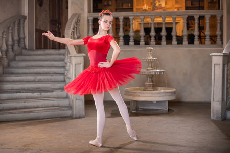 A young ballerina in a red tutu is dancing against the background of the theatrical scenery of the palace.の写真素材