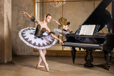 Young ballerina in a white tutu dancing on a beautiful old piano in a vintage interiorの写真素材