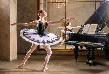 Young ballerina in a white tutu dancing on a beautiful old piano in a vintage interiorの写真素材