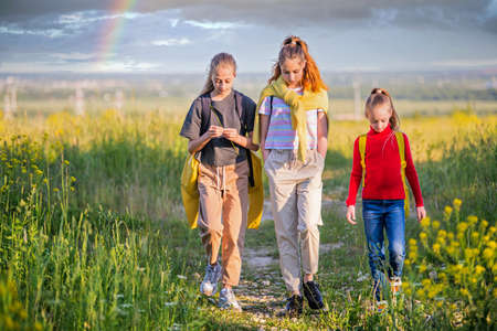 Group of girls walking in nature with backpacks on the background of sunset, active healthy lifestyleの写真素材