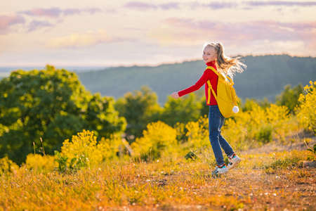 Girl child running in the evening with a backpack in nature on the background of a flowering meadow, steppe, active healthy lifestyleの写真素材