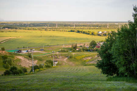 Panoramic view from the mountain to a small rural settlement among fields and forests at sunset in summer.の写真素材