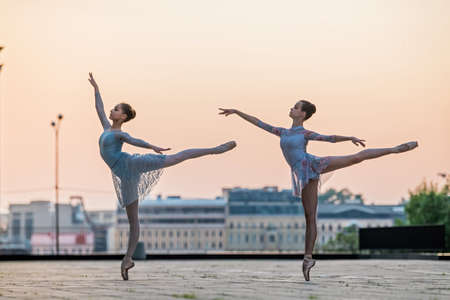 Two young ballerinas dancing in pointe shoes in the city against the backdrop of the sunset skyの写真素材