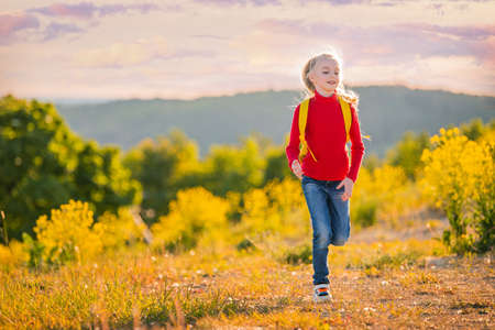 Girl child running in the evening with a backpack in nature on the background of a flowering meadow, steppe, active healthy lifestyleの写真素材