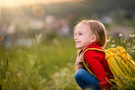 portrait of a child girl in a red jumper with a backpack traveling on a summer evening against the backdrop of a landscape.の写真素材