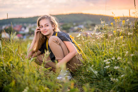 Portrait of a teenage girl with a backpack traveling on a summer evening against the backdrop of a landscape and sunset.の写真素材