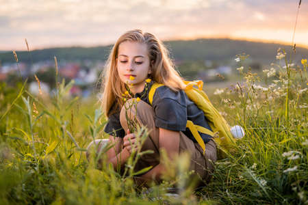 Portrait of a teenage girl with a backpack traveling on a summer evening against the backdrop of a landscape and sunset.の写真素材