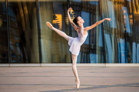 young ballerina in a white leotard dancing on pointe shoes against the backdrop of a cityscapeの写真素材