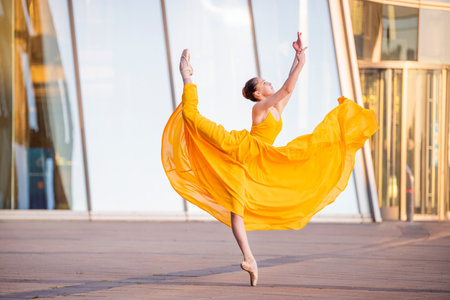 a young ballerina in a long flying yellow dress is dancing against the backdrop of a cityscapeの写真素材