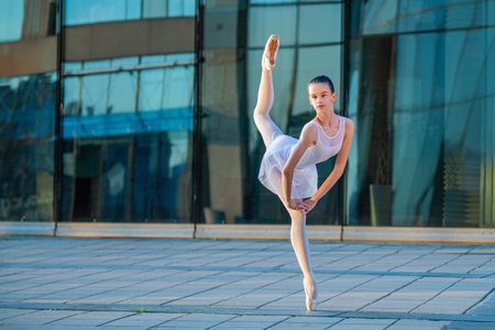 young ballerina in a white leotard dancing on pointe shoes against the backdrop of a cityscapeの写真素材