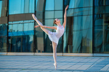 young ballerina in a white leotard dancing on pointe shoes against the backdrop of a cityscapeの写真素材